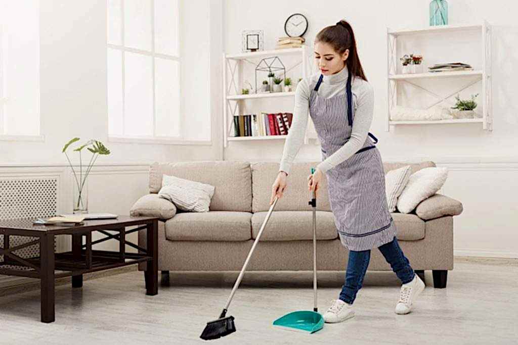 Efficient professional maid sweeping living room floor with broom and dustpan.